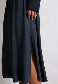 Marineblaues Kleid mit knielangem Schnitt, Seitenschlitzen, glatter Textur und kontrastierenden Ärmeldetails.
