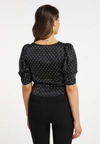 Schwarze Satinbluse mit Puffärmeln, kompliziertem silbernem geometrischem Muster und rundem Halsausschnitt. Glatte Textur und figurbetontes Design.
