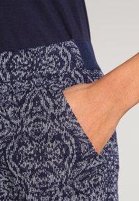 Marinblå mönstrade byxor med en texturerad tyg, med en kontrasterande midja och sidoficka, som framhäver en geometrisk design i ljusare nyanser.