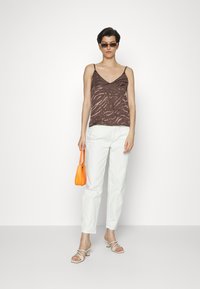 Camisola castanha com padrão e alças finas, combinada com calças brancas de perna reta e uma bolsa laranja. Sandálias de salto brancas completam o visual.
