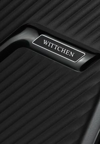 Černý cestovní kufr s texturovaným, vroubkovaným designem. Má lesklou černou rukojeť a kovovou destičku označenou "WITTCHEN." Hladký povrch.