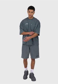 Grå oversized t-shirt med en lomme, parret med matchende grå shorts. Båret med grå høje sneakers og hvide sokker. Enkel, afslappet design.