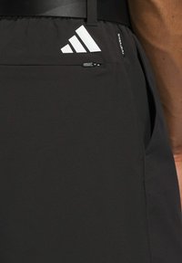 Czarne sportowe szorty z boczną kieszenią na zamek, elastycznym pasem i białym logo Adidas po lewej stronie. Gładki, lekki materiał.