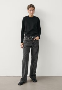 Black long-sleeve sweater, high neckline, paired with high-waisted gray jeans, featuring a relaxed fit and a black belt. Black ankle boots.