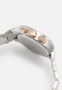 Montre en acier inoxydable argenté avec un accent en or rose, dotée de trois boutons-poussoirs sur le côté et d'un bracelet interchangeable texturé.