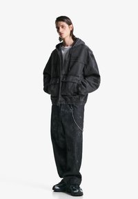 Grijze hoodie-jack met een rits, twee voorkiezen en een verstelbare trekkoord; gecombineerd met losse zwarte broek met een kettingaccent.