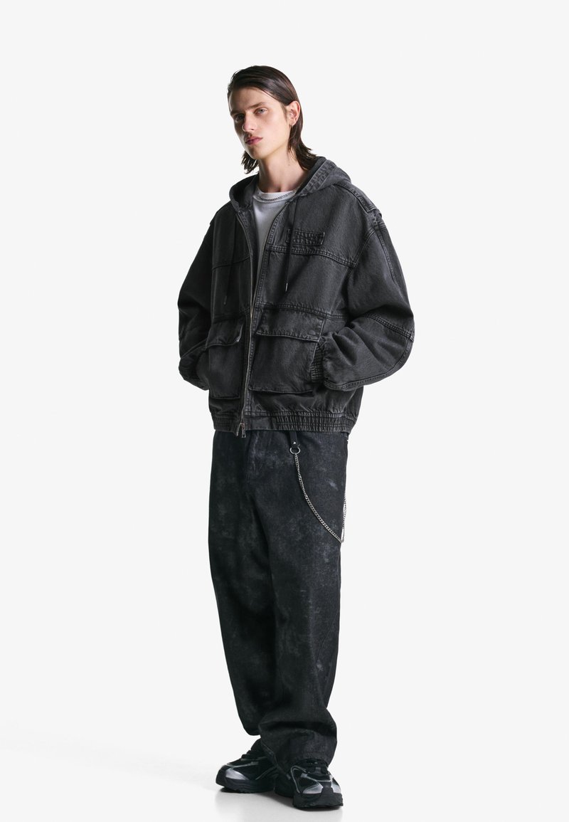Grijze hoodie-jack met een rits, twee voorkiezen en een verstelbare trekkoord; gecombineerd met losse zwarte broek met een kettingaccent.