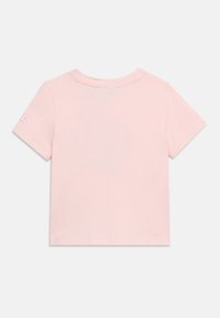 Ροζ ανοιχτόχρωμο κοντομάνικο μπλουζάκι απλωμένο, που δείχνει την πίσω πλευρά με ένα μικρό ροζ και λευκό σχέδιο στο αριστερό μανίκι.