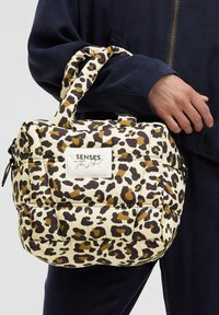 Leopard print handbag with padded design, featuring black and brown spots on a cream background. Includes a white label and short handles.