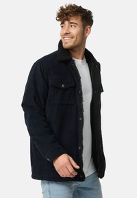 Marineblauwe corduroy jas met een zwarte fleece kraag, voorzakken met knopen en een ritsclosure; textiel met structuur en een relaxte pasvorm.