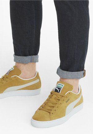 Sneakers gialli in suede con accenti bianchi, dotati di suola in gomma, punta tondeggiante e design classico con lacci. Etichetta verde vicino al tallone.