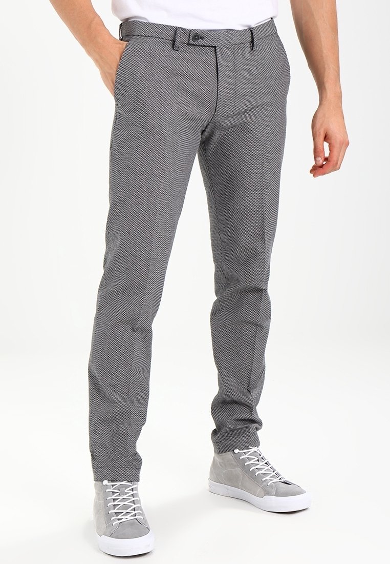 Homme portant un pantalon gris slim texturé avec poches avant et des baskets montantes grises avec lacets blancs, debout avec une main dans la poche.