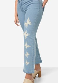 Vaqueros de denim azul con estampados de mariposas blancas a lo largo de la pierna izquierda, con un diseño de pierna recta y una cintura de altura media.