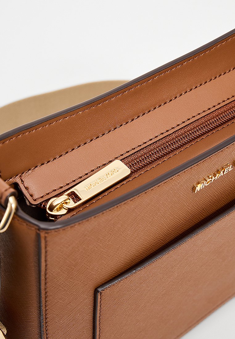 Intérieur d'un sac à main en cuir marron avec une poche zippée et des finitions en or. Présente une texture subtile et une poche extérieure bien visible.