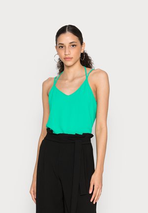 Top verde sem mangas feito de tecido leve, com decote em V e alças finas, combinado com calças pretas de cintura alta e um cinto atado.