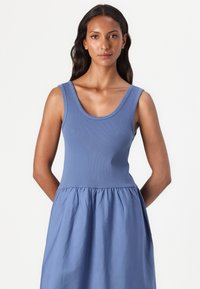 Blue sleeveless dress with a fitted ribbed bodice and a gathered, flowing skirt. The fabric has a smooth texture and a lightweight appearance.