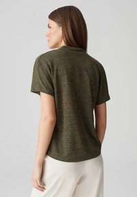 Top verde oliva a maniche corte realizzato in materiale testurizzato, con scollatura rotonda e vestibilità rilassata, mostrato da dietro.