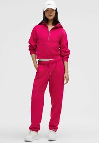 Ljusröd kort hoodie med en framficka och half dragkedja, matchad med joggerbyxor som har elastisk midja och ärmslut.