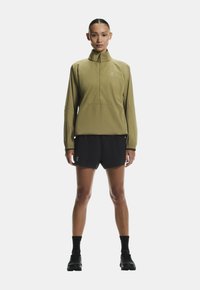 Világos olivazöld pulóver magas gallérral és félcipzárral, fekete rövidnadrággal párosítva. Jellemzői közé tartozik az elasztikus mandzsetta és egy kis logó az oldalon.