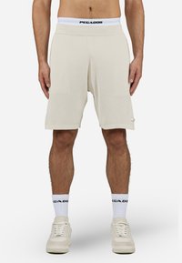Beige ribbed shorts with a comfortable waistband, featuring a black "PEGADOR" logo. Worn with white socks and light-colored sneakers.