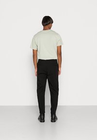 T-shirt verde chiaro a maniche corte e pantaloni neri affusolati con tasche laterali, indossati con stivaletti neri alla caviglia, visti da dietro.