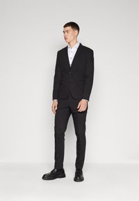 Black suit with a fitted design, white shirt underneath, black shoes, and a smooth texture. Simple button detail on the shirt.