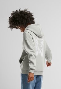 Ljusgrå hoodie med en rymlig huva, med en reflekterande fjärilsdesign och texten "GOOD KARMA" på baksidan. Mjuk textur.