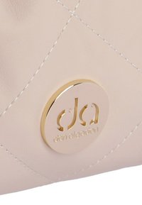 Bolso rosa acolchado de cuero con un logo circular dorado con letras recortadas y detalles de costura en contraste blanco.