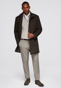 Abrigo de ante marrón sobre un suéter gris claro, combinado con pantalones gris claro y botas de ante marrón, con un diseño elegante y detalles mínimos.