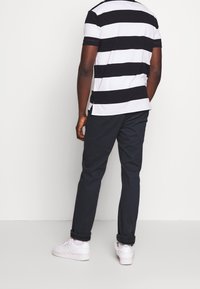 Polo à manches courtes rayé en noir et blanc, associé à un pantalon sombre et des baskets blanches. Vue de dos, montrant les poignets retroussés.