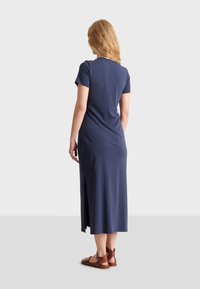 Tummansininen, lyhythihainen, maksimekko sivuleikkauksilla. Pehmeä, venyvä materiaali ja istuva siluetti, yhdistetty ruskeisiin remmisandaaleihin.