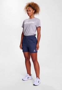 Grå t-shirt med texten "hummel", kombinerad med marinblå shorts med elastisk midja och logotyp. Vita sportskor fulländar outfiten.