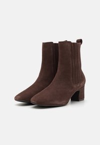 Botines de ante marrón con punta afilada, tacón cuadrado, paneles laterales elásticos y una lengüeta, que cuentan con una textura suave y un diseño elegante.