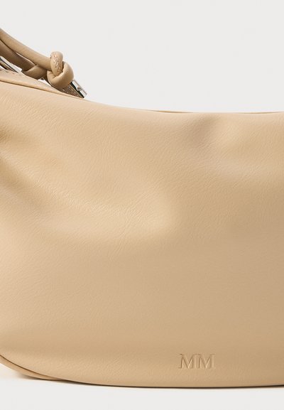 Sac à'épaule en cuir beige avec une texture lisse et un éclat subtil, arborant un logo "MM" en relief et une conception arrondie.