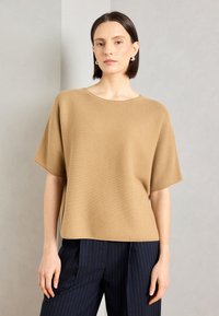 Top scurt din tricot bej, cu o croială lejeră și decolteu rotund. Combinat cu pantaloni în dungi navy. Textură netedă și material ușor.