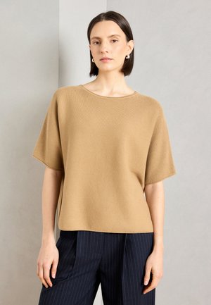 Top corto a maniche corte beige in maglia con vestibilità rilassata e scollatura rotonda. Abbinato a pantaloni navy con righe sottili. Texture liscia e materiale leggero.