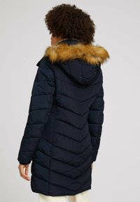 Granatowa pikowana kurtka puchowa z kapturem obszytym futerkiem, z przeszyciami w kształcie jodełki i bocznymi kieszeniami. Gładka faktura i regulowany dół.