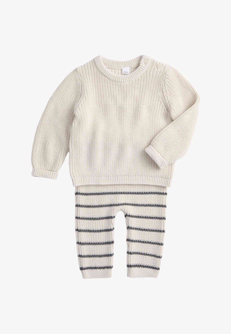 Maglione crema lavorato a maglia con scollo rotondo e due bottoni sulle spalle, abbinato a pantaloni a righe crema e grigio, con una texture morbida.
