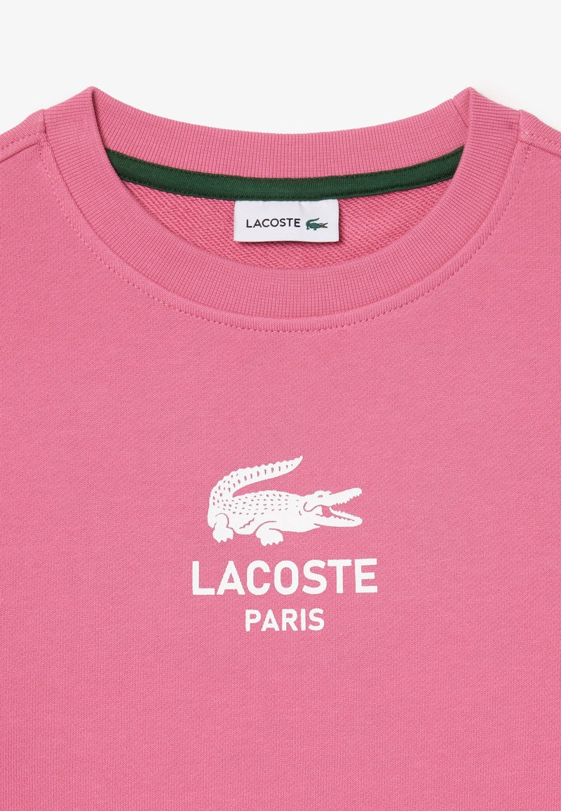 Rosa Baumwoll-T-Shirt mit Rundhalsausschnitt, ausgestattet mit einem weißen Krokodil-Logo und dem Text "LACOSTE PARIS", das von einem grünen Kragen akzentuiert wird.