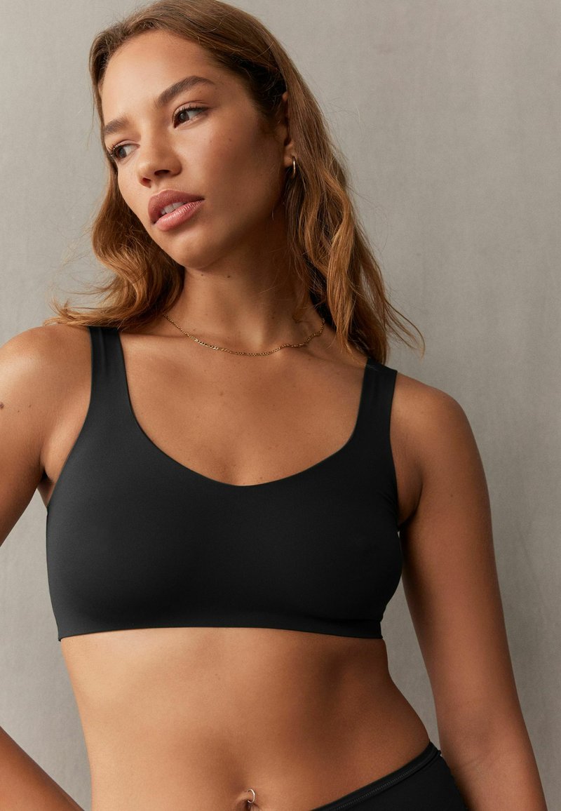 Fekete bralette széles pántokkal, kerek nyakkivágással, sima anyagból készült. Minimalista dizájn, látható varratok vagy fém részletek nélkül.
