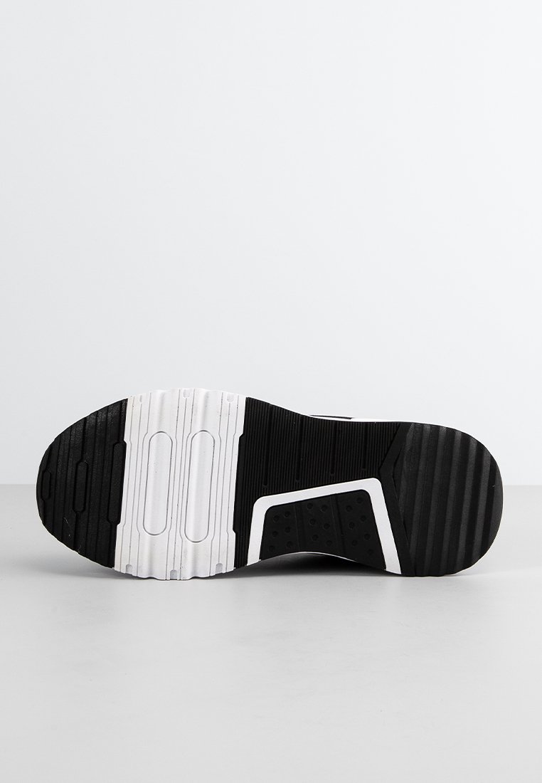 Suela de zapatilla negra con superficie de goma texturizada, acentos blancos, agujeros de drenaje y canales alargados para tracción.