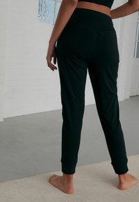 Pantaloni jogger neri, aderenti, con vita alta, gambe affusolate e polsini a coste. Tessuto morbido con una texture liscia.