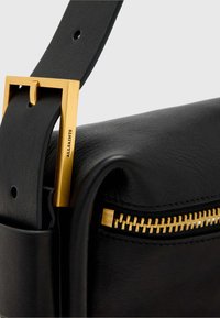 Čierna kožená taška so zlatým kovaním, vybavená zipsovým zapínaním a plochým remienkom s obdĺžnikovou prackou. Hladká textúra, minimalistický dizajn.