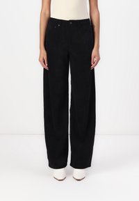 Szerokie czarne spodnie z korduroyu z pionowym połhą, pięcioma kieszeniami i wysokim stanem, w połączeniu z białymi botkami za kostkę.