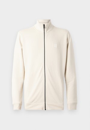 Felpa zip con collo alto di un beige chiaro, maniche lunghe e un piccolo logo sul petto. Realizzata in un materiale morbido e con texture.