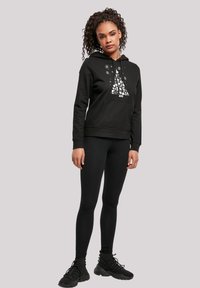 Felpa nera con un design grafico di un albero, tasca frontale e cappuccio con coulisse regolabile, abbinata a leggings neri e scarpe da ginnastica.