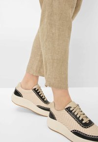 Baskets beiges et noires avec un motif en chevron, tige texturée et semelle blanche striée. Lacets de la même couleur.