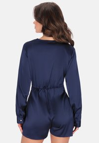 Námořnický saténový overal s dlouhými rukávy, elastickým pasem a knoflíkovými manžetami. Hladká textura s volným střihem a krátkým spodkem.