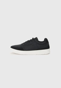 Black athletic shoe featuring smooth synthetic upper, textured accents, lace closure, and a white rubber sole with a patterned tread.