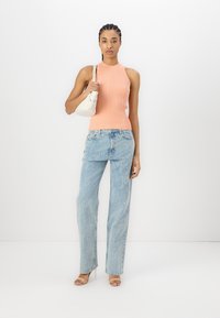 Top a righe in corallo, jeans in denim chiaro con motivo testuale, sandali con tacco trasparente, mentre tiene una borsa rotonda bianca.